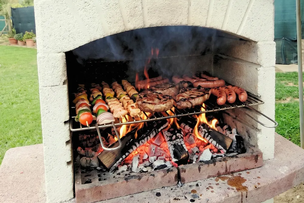 Il barbecue in muratura acceso, con spiedini, bistecche e salsicce sulla griglia