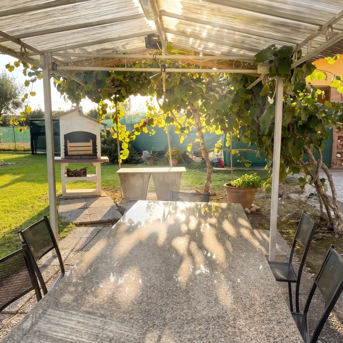 Il pergolato di Lemon Villa: il grande tavolo in granito sotto la pianta rampicante, con il barbecue in muratura sul prato