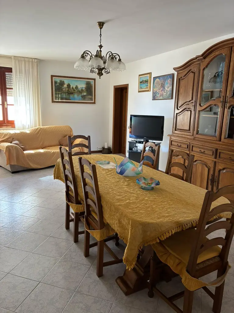La sala con il grande tavolo in legno, il divano, la televisione e la credenza